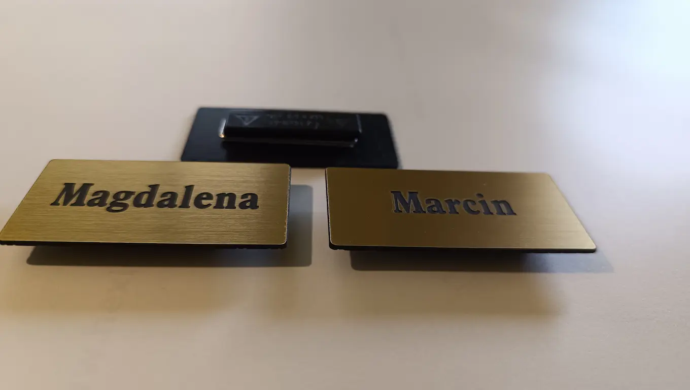 Złote identyfikatory z laminatu grawerskiego z imionami na przypince magnetycznej