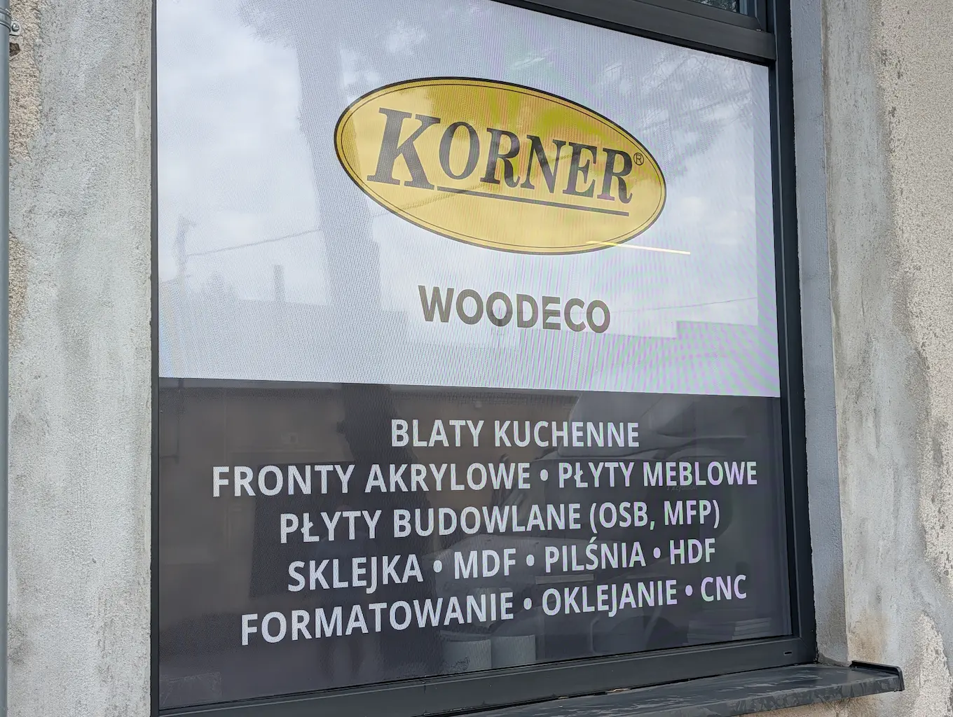 Oklejanie witryny folią OWV One Way Vision z logo KORNER WOODECO i ofertą płyt meblowych