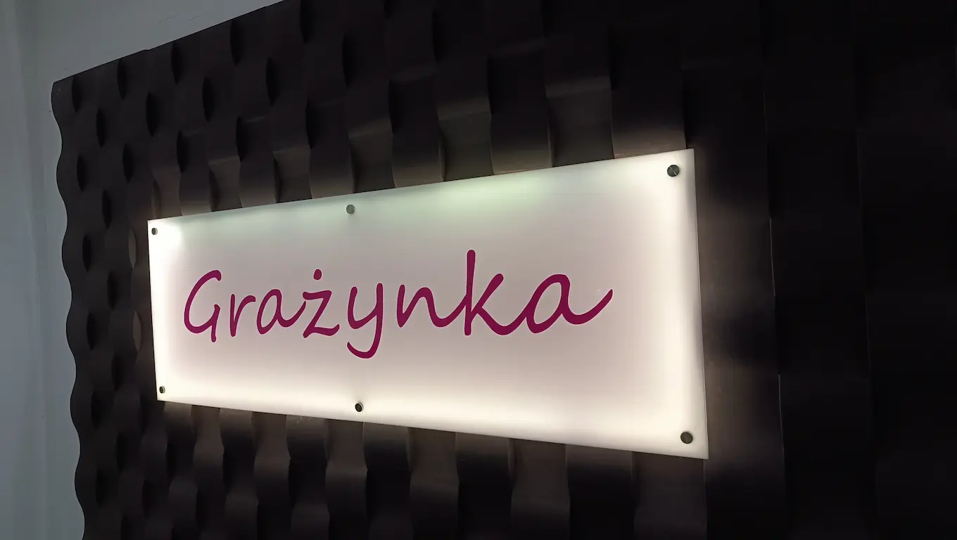 Podświetlany szyld z mlecznej plexi z logo Grażynka na ścianie lamelowej LED