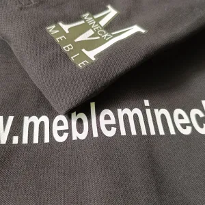 Znakowanie odzieży firmowej folią flex dla Minecki Meble – biały nadruk logo i adresu www na ciemnej tkaninie