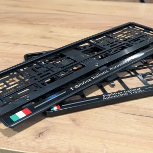 Czarne ramki pod tablice rejestracyjne oklejone folią polimerową z napisem Fabbrica Italiana Automobili Torino i flagą Włoch