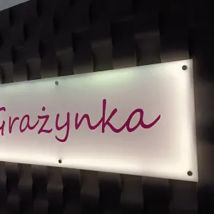 Podświetlany szyld z mlecznej plexi z logo Grażynka na ścianie lamelowej LED